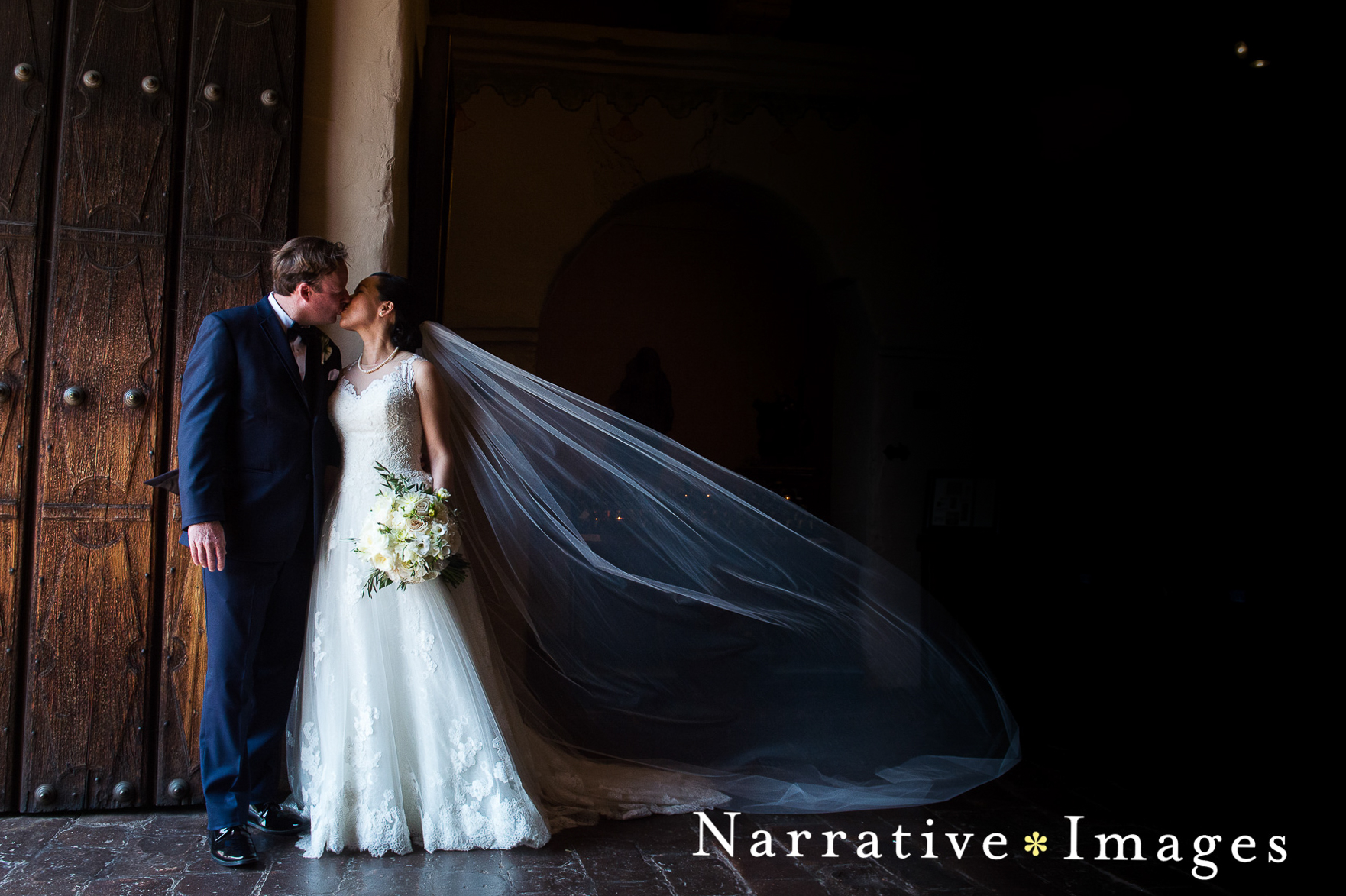Bride and groom kiss in front of doors at Mission San Diego de Alcala