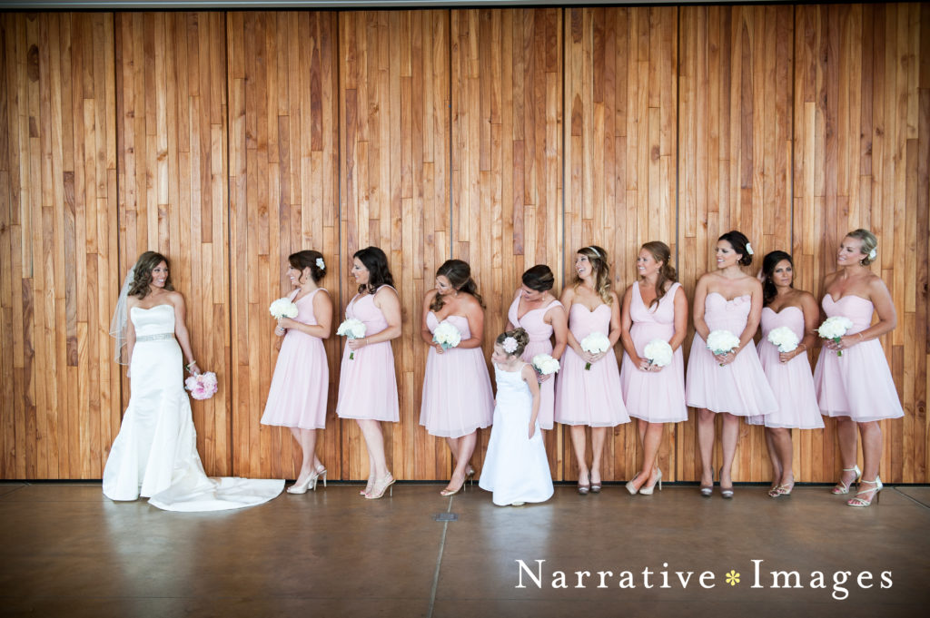 Bride and Bridemaids in pink dresses in front of wood wall at Scripps Seaside Forum in La Jolla, California.