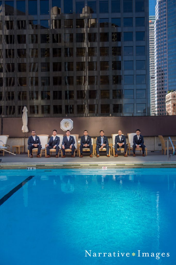 Groomsmen sit in pool chairs dressed in suits in downtown LA before their classic wedding