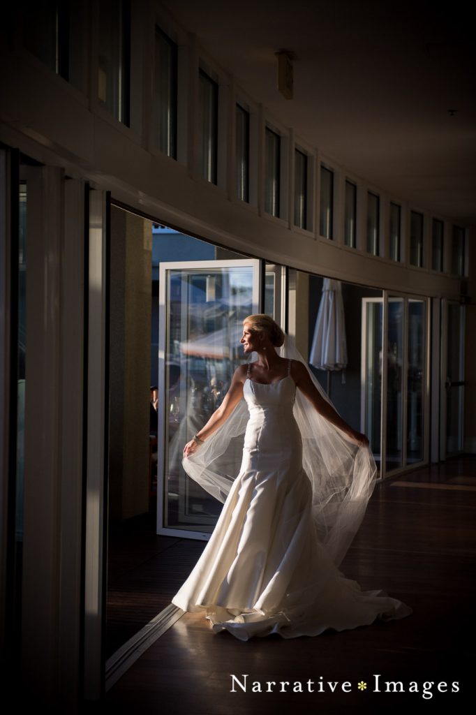 Bride wearing a satin wedding dress and long veil walks through L'Auberge lobby