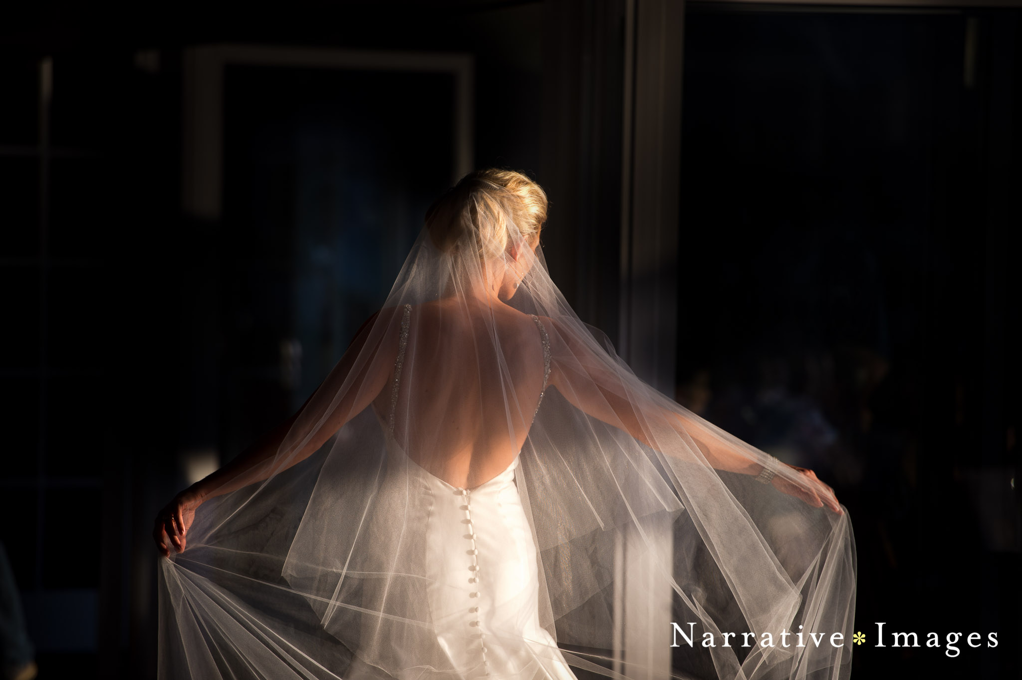 long bridal veil catches wind in sunlight as bride walks through hotel lobby at L'auberge wedding venue