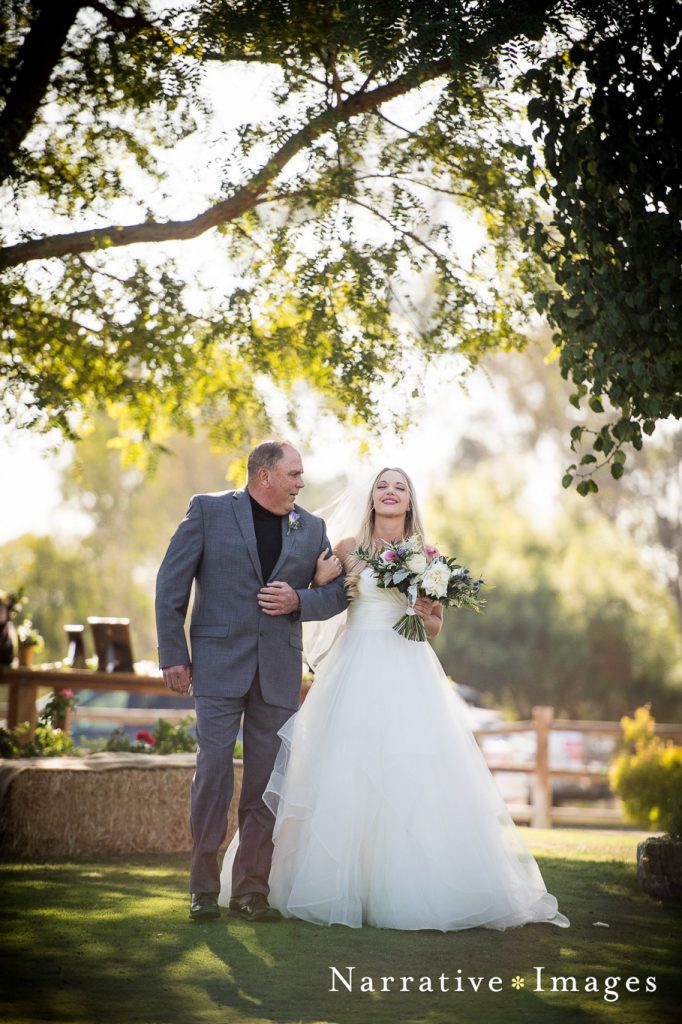 father of the bride walks his daughter down the isle at outdoor wedding ceremony