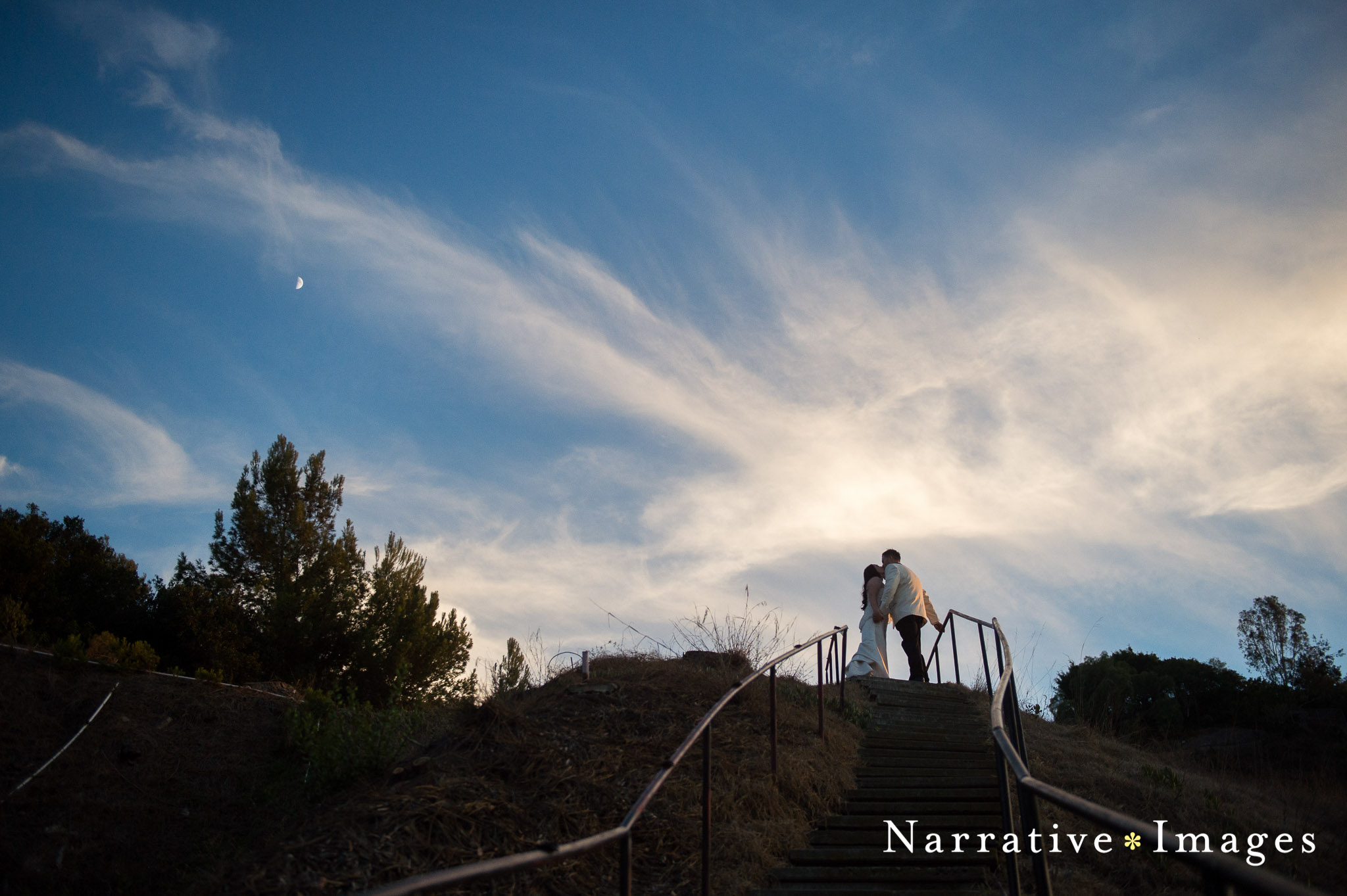 Couple kiss at top of outdoor staircase with sky and clouds at First Methodist Church in San Diego