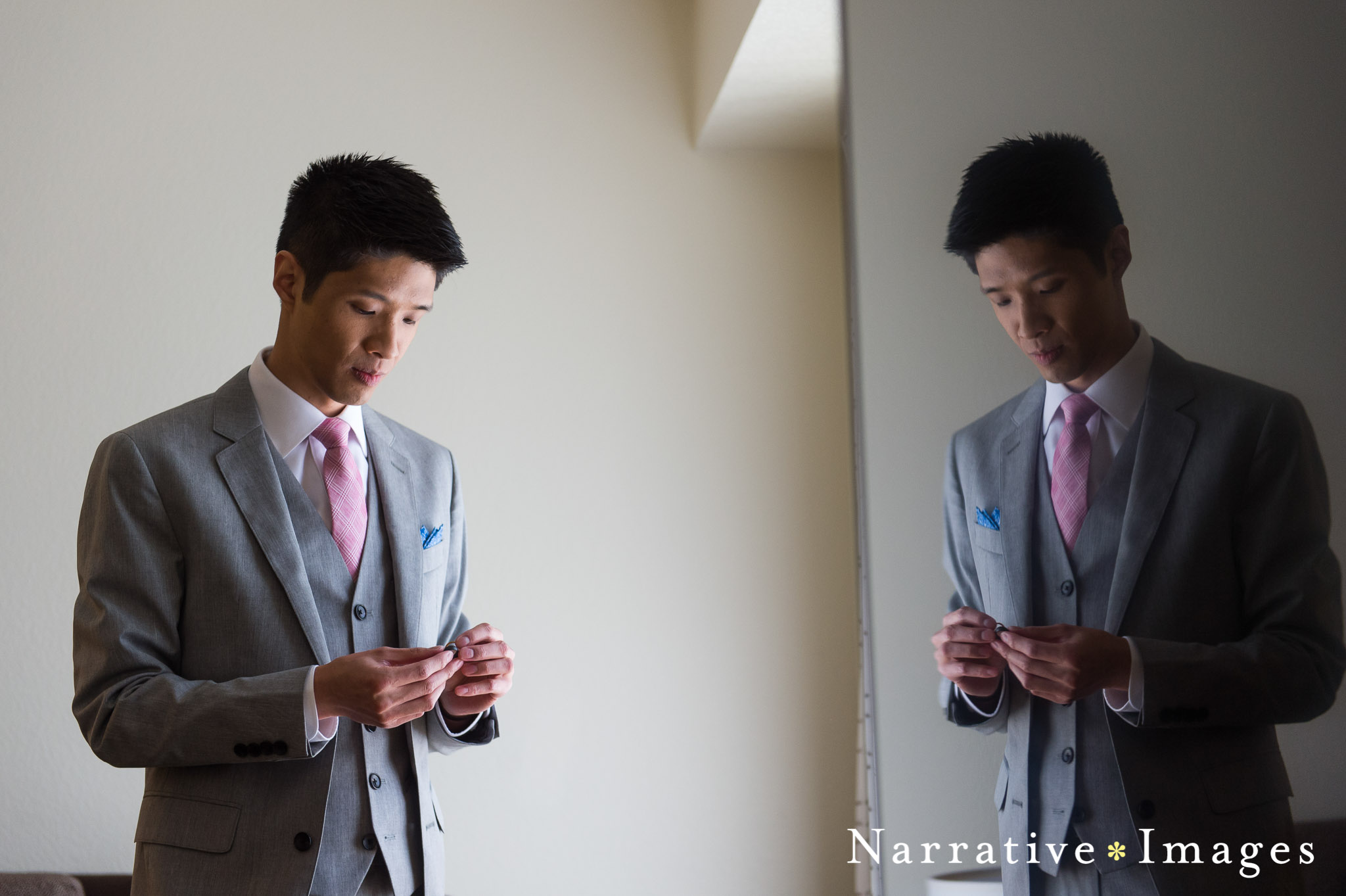 Groom looks down at wedding band dressed in pink tie and grey suit