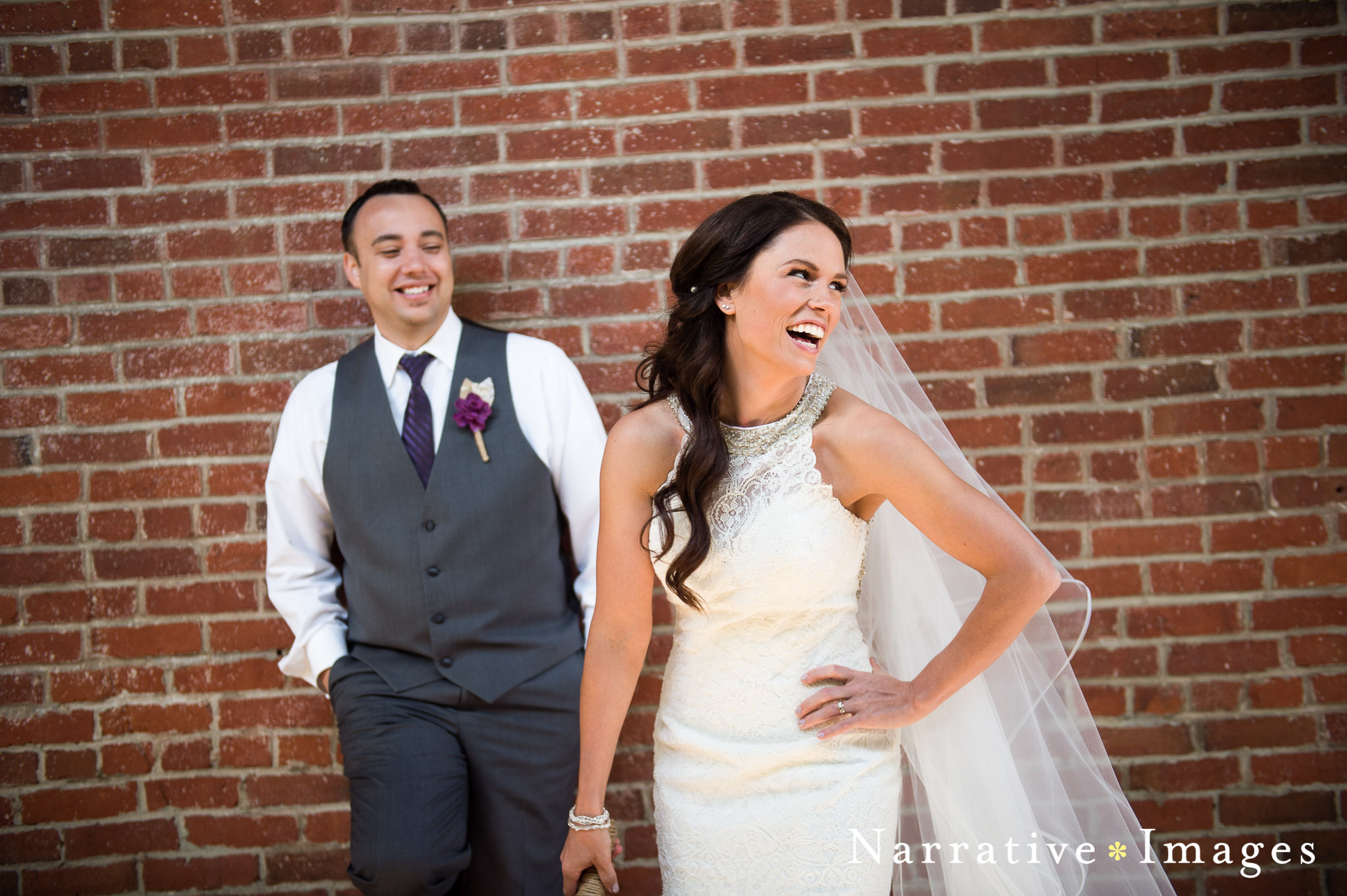 Bride laughing with Groom in background standing against brick wall in downtown temecula
