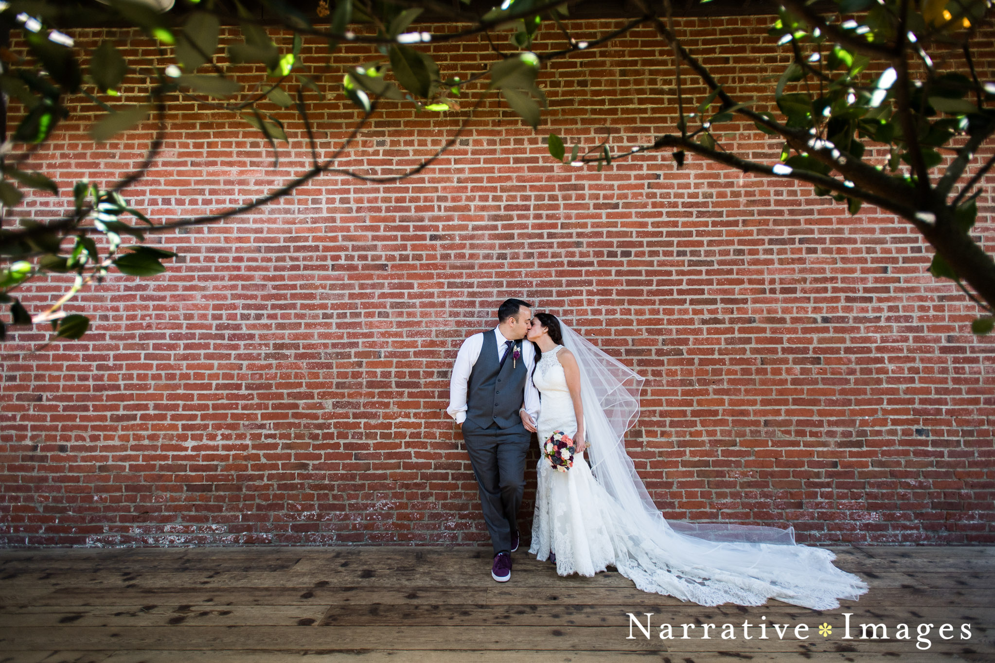 Bride and Groom kissing standing against brick wall in downtown temecula