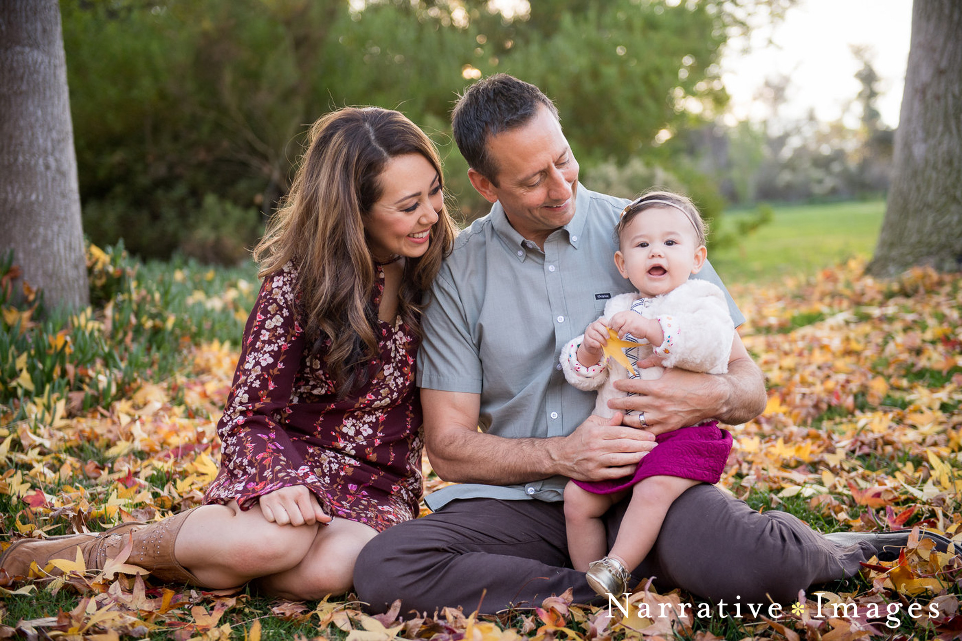 candid portrait of two parents with toddler girl in fall leaves