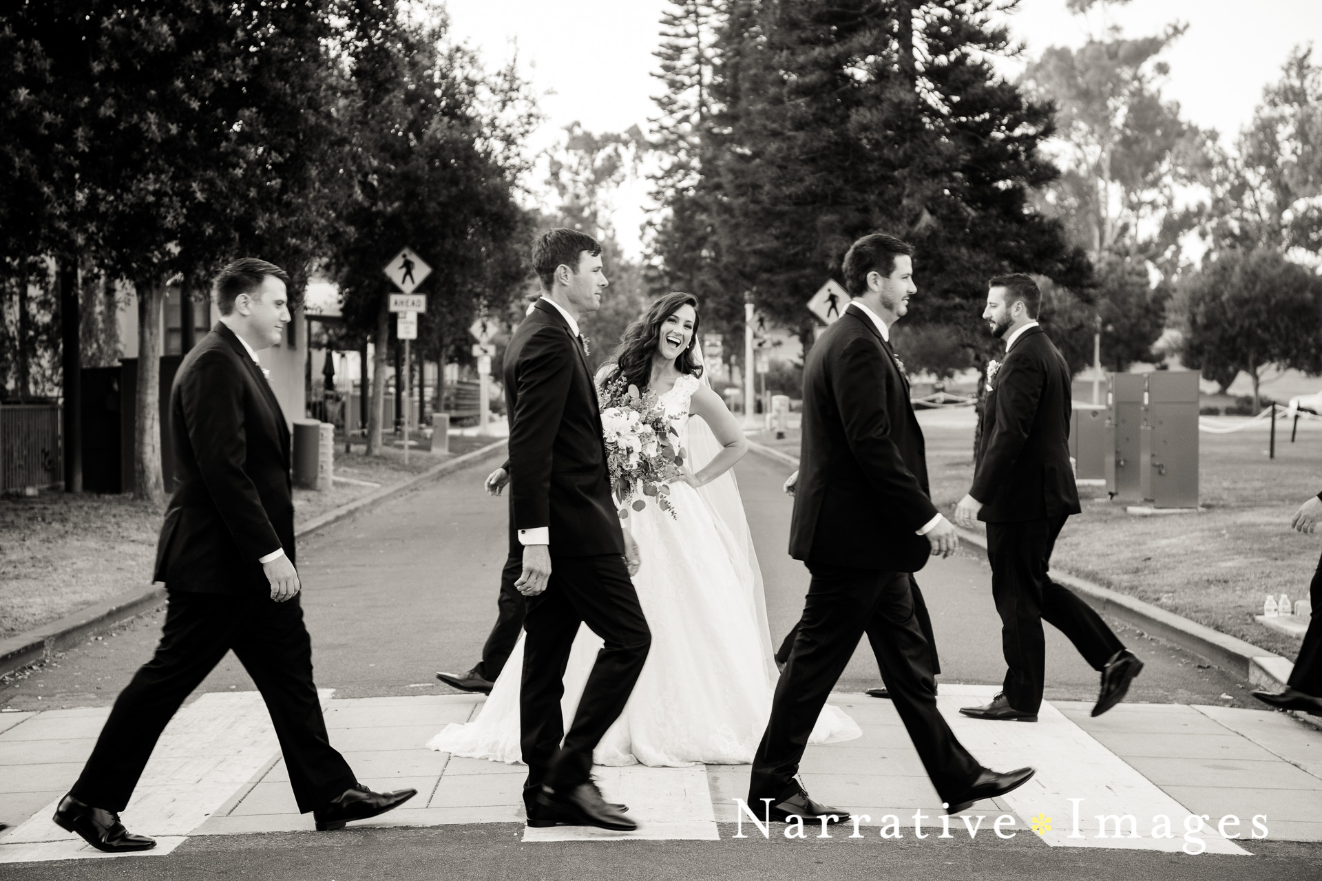 Bride smiles between groomsmen walking by on crosswalk