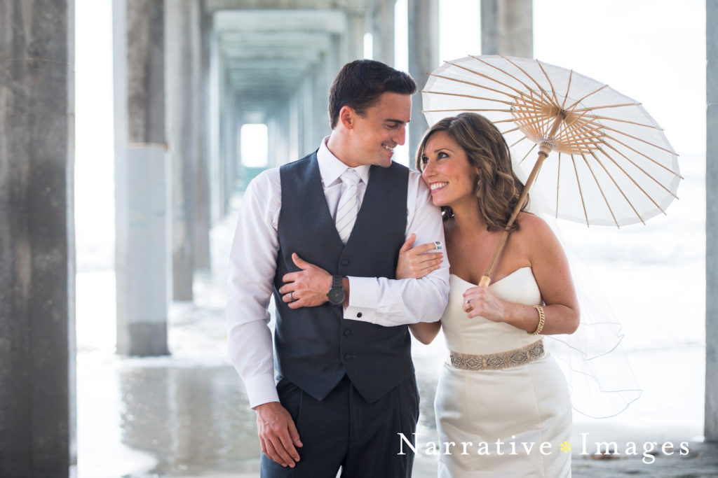 Bride and Groom with a parasol, walk arm-in-arm under Scripps Pier in La Jolla, California
