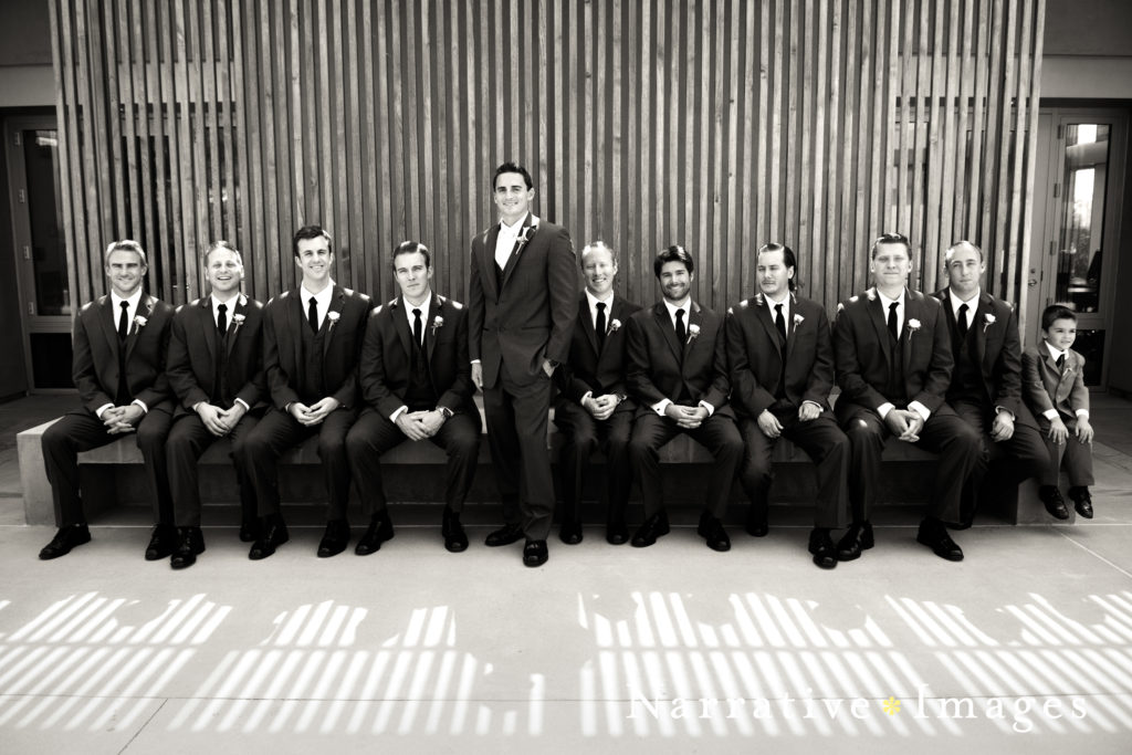 Groomsmen pose for photo in front of wood slats in black and white photo at Scripps Seaside Forum in La Jolla, California