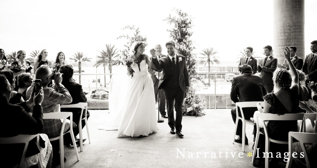 Bride and groom link arms in celebration as they walk down the aisle at The Lane wedding venue in San Diego.