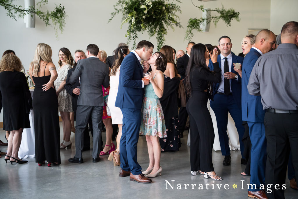 Candid photo of two wedding guests kissing amongst a crowd at a wedding reception at The Lane in San Diego